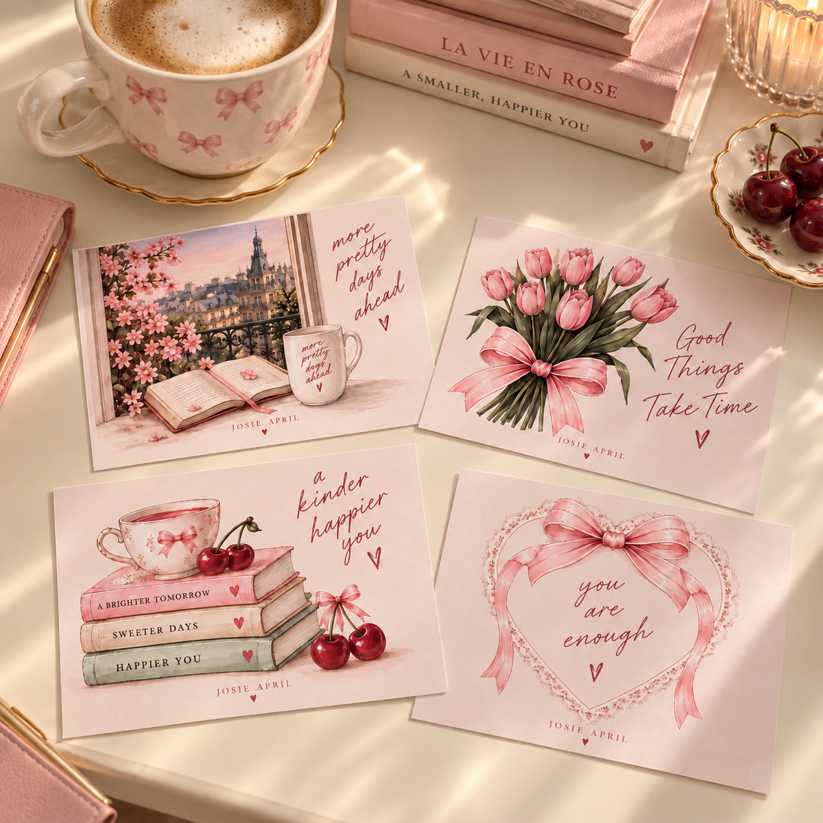 Vier JOSIE APRIL Postkarten mit rosa Kaffeetasse, Büchern und Kirschen auf hellem Tisch